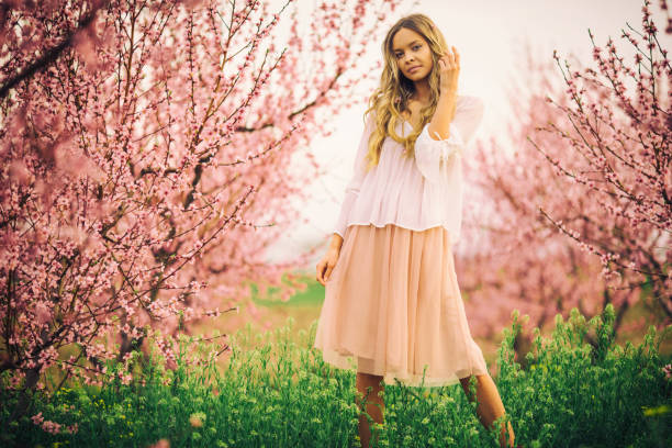 Amazing beautiful young woman and fashion model enjoying life and posing in cherry alley at spring while threes are with flower blossom