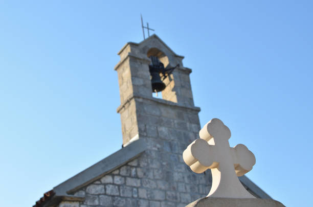 Marble cross of a grave with a church belfry behind it