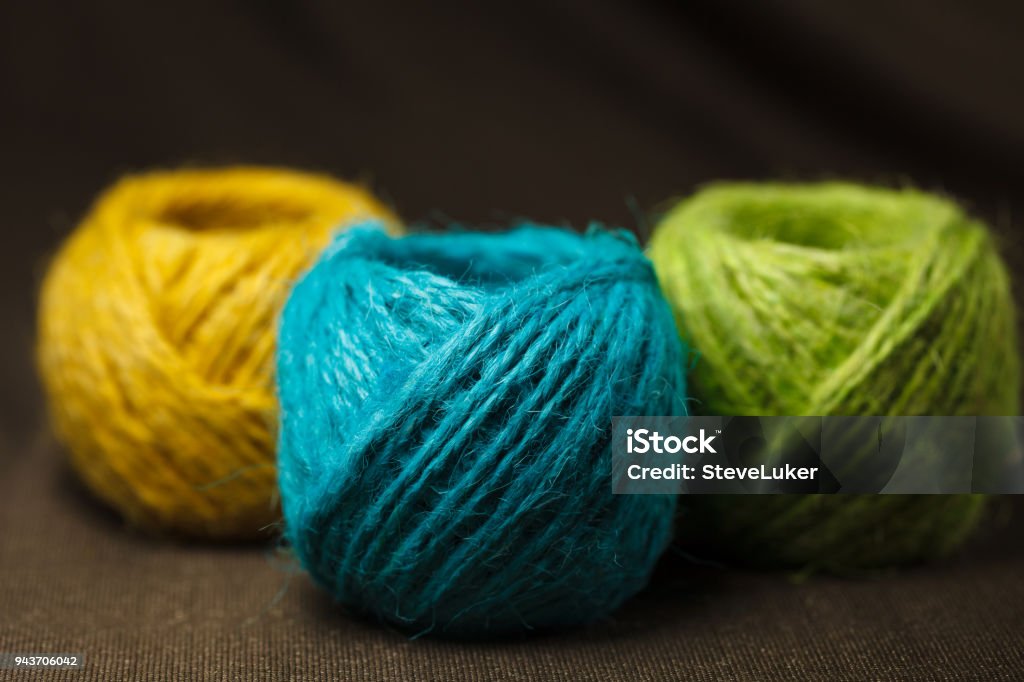 Three colorful balls of hemp cotton a brown surface Blue, green, and yellow hemp cotton balls. Ball Of Wool Stock Photo