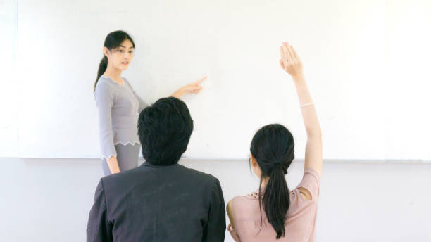 istock asian girl points hand on the whiteboard wall with the student sit on front of classroom 943709486