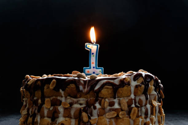 istock One flaming candle on birthday cake on black background 943712776