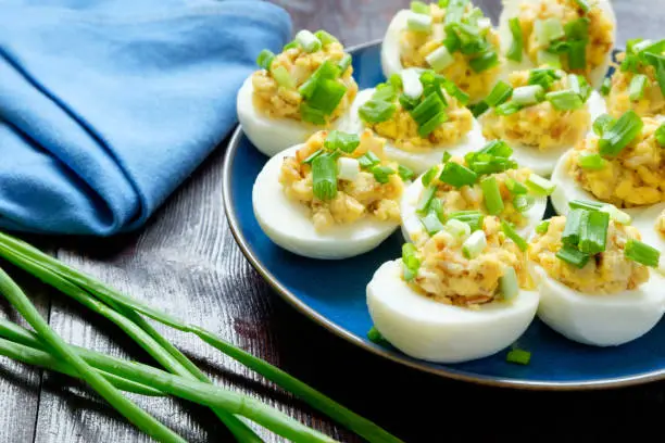 Eggs stuffed with green onion on a blue plate on a wooden background, close up