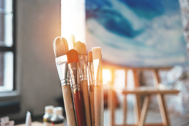 istock Closeup of artist paintbrushes and studio interior. Blurred background. Workshop or art class. Creative concept. Flare effect 943712830