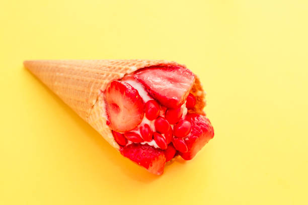 istock Ice cream with red strawberries divided in half and red sweets in waffle cone on yellow surface 943722258
