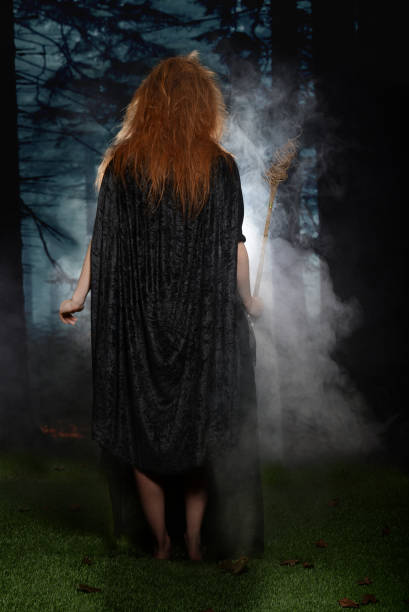 istock witch walking into the forest holding her wand with fog 943723196