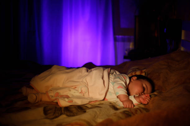 Child sleeping and dreaming in parents bed in dark yellow calm light. Selective focus. Cute little girl is sweetly sleeping in bed. Image with selective focus and toning