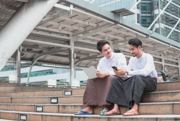 잘생긴 두 아시아 사람이 듣는 음악을 계단에 앉아 행복은 - 사롱 뉴스 사진 이미지