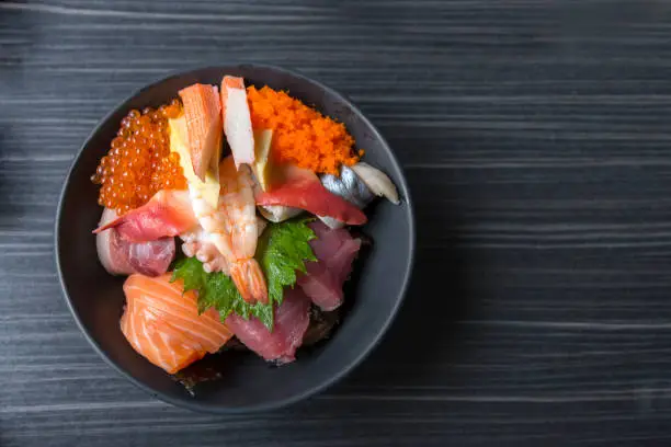 Premium fresh raw seafood mixed rice bowl (Kaisen-don/ Japanese tasty food), Japanese Rice with sashimi of tuna, Maguro, Otoro, salmon, squid and ikura (Salmon eggs) on wood background