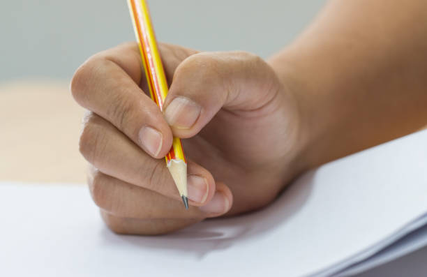 istock Hands with pencil over application form, Students taking exams, writing examination room with undergraduate students inside. Student sitting learning lessons doing final exam in classroom. 943735668