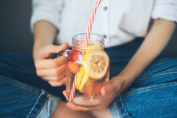 cropped shot of young woman drinking home made fresh summer drink from mason jar with straw stock photo