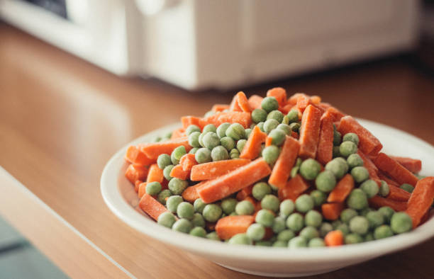 frozen vegetables on plat near microwave, kitchen indoor. Vegan food stock photo