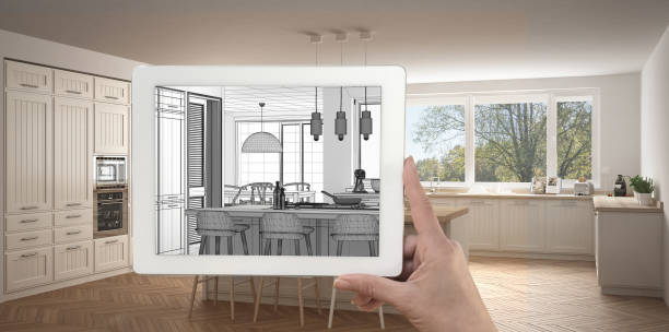 istock Hand holding tablet showing kitchen sketch or drawing. Real finished modern kitchen with island and stools in the background, architecture interior design presentation 943758822