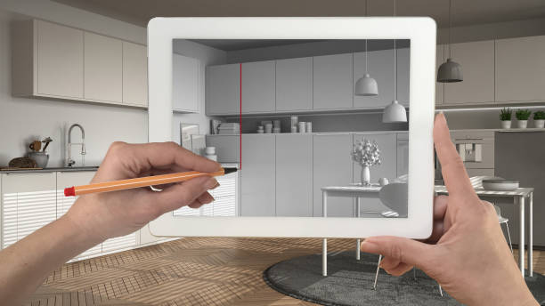 istock Hands holding and drawing on tablet showing modern kitchen sketch. Real finished minimalist white and wooden kitchen in the background, architecture interior design presentation 943762506