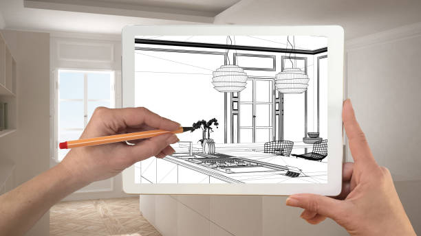 istock Hands holding and drawing on tablet showing modern kitchen CAD sketch. Real finished minimalist white and wooden kitchen in the background, architecture interior design presentation 943771896