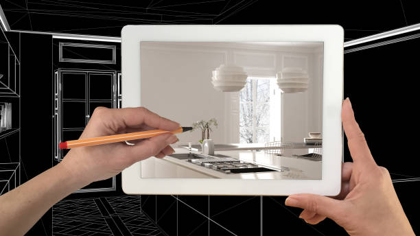 istock Hands holding and drawing on tablet showing real finished minimalist white kitchen. Modern kitchen CAD sketch in the background, architecture interior design presentation 943772020