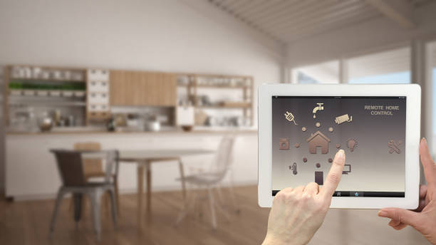 istock Smart remote home control system on a digital tablet. Device with app icons. Blurry interior of white kitchen in the background, architecture design 943776864