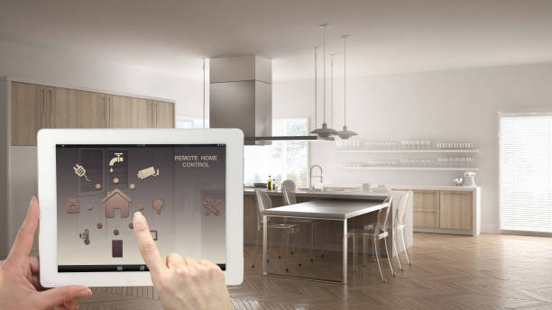 istock Smart remote home control system on a digital tablet. Device with app icons. Interior of minimalist white and wooden kitchen in the background, architecture design. 943778976