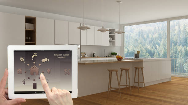istock Smart remote home control system on a digital tablet. Device with app icons. Interior of minimalist white and wooden kitchen in the background, architecture design. 943778996