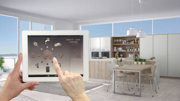 istock Smart remote home control system on a digital tablet. Device with app icons. Interior of minimalist white kitchen in the background, architecture design. 943779046