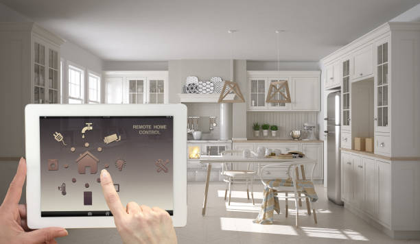 istock Smart remote home control system on a digital tablet. Device with app icons. Interior of scandinavian white and wooden kitchen in the background, architecture design. 943779298