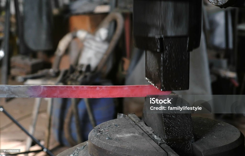 Using pneumatic hammer to shape hot metal. Making the sword out of metal. Side view. Using pneumatic hammer to shape hot metal. Making the sword out of metal. Barracks Stock Photo