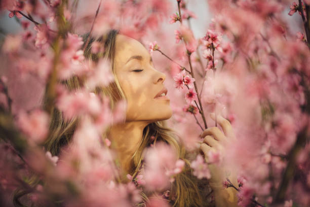 Closeup portrait of beautiful young woman with healthy skin who enjoying life and standing among cherry branches with flower blossom. She is very happy and cheerful