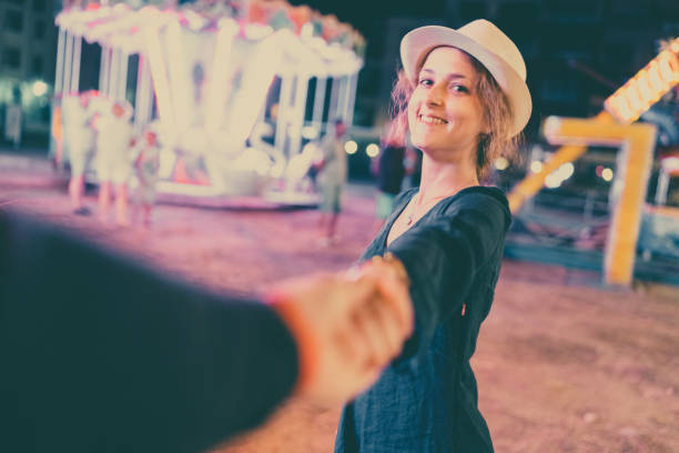 Smiling woman taking her boyfriend to amusement park at night