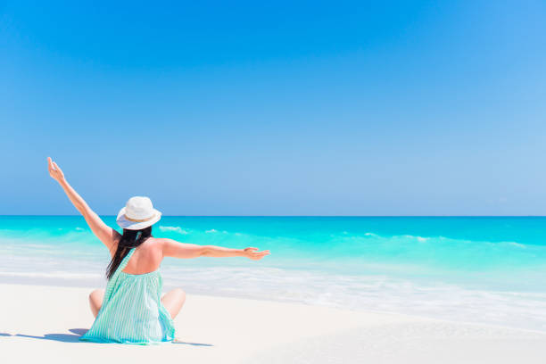 Young happy woman in swimsuit on white beach. Beautiful model in bikini sitting down.