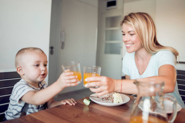 istock Little boy eating cake and drinking orange juice with his mum 943851586