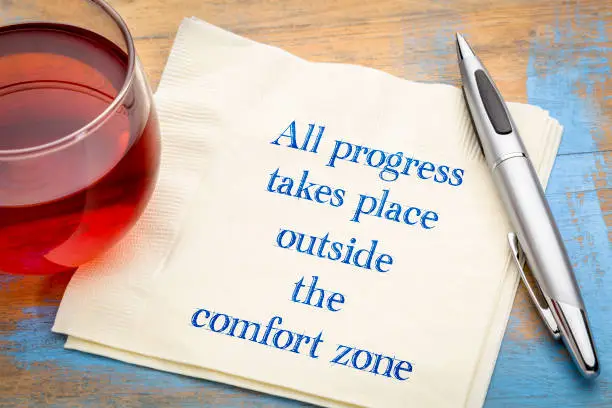 All progress takes place outside the comfort zone - inspiraitonal handwriting on a napkin with a cup of tea