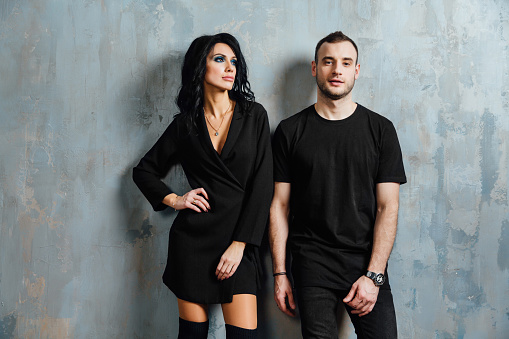 Young stylish beautiful gorgeous couple, against the gray wall loft in the studio or at home. Valentine's Day. black fashionable clothes. Exquisite clothes, dark dress.