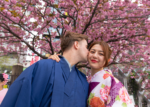 Young couple in kimono kissing under cherry tree