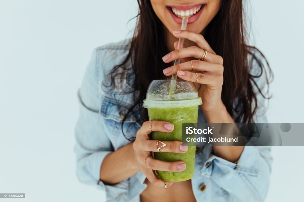 Smiling woman drinking fresh juice Close up of smiling woman drinking fresh juice with straw on white background. Female having a glass of fruit juice and smiling. Smoothie Stock Photo