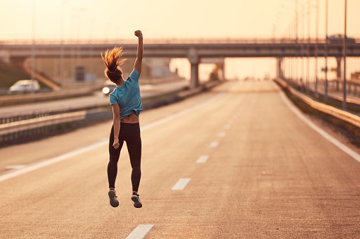 Image of a young sportswoman jumping for joy and with arms up celebrating success.
