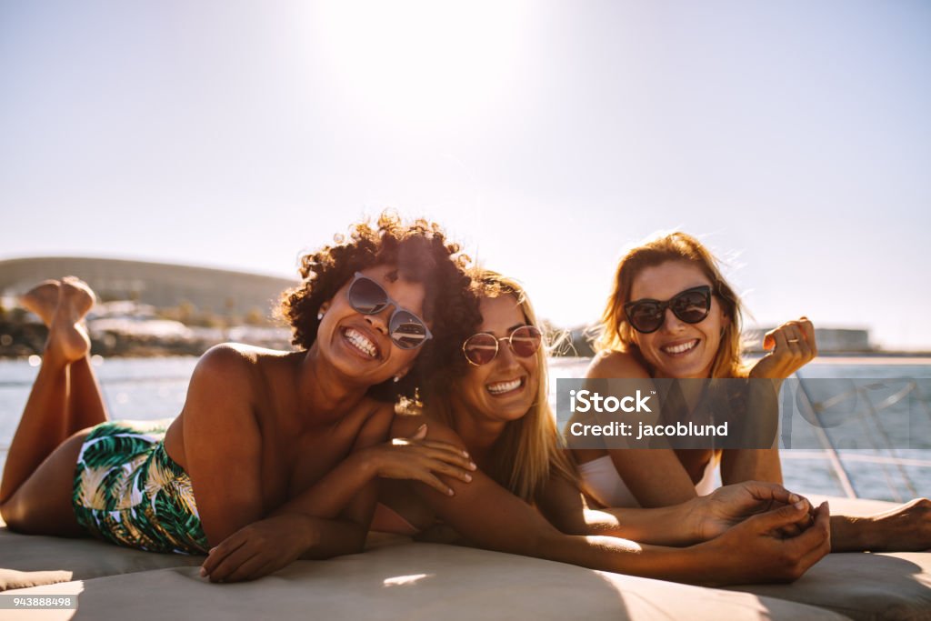 Group of beautiful women relaxing on a yacht deck Group of beautiful women relaxing on a yacht deck. Three female friends sunbathing on small boat looking at camera and smiling. Friendship Stock Photo