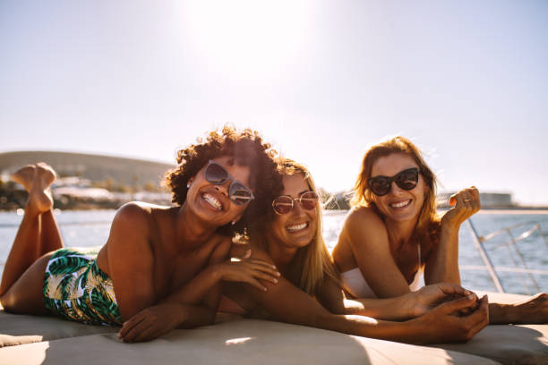 Group of beautiful women relaxing on a yacht deck Group of beautiful women relaxing on a yacht deck. Three female friends sunbathing on small boat looking at camera and smiling. sunbathing stock pictures, royalty-free photos & images