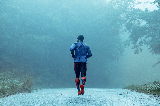 Motivated young man running in the rain. Rear view. Copy space.