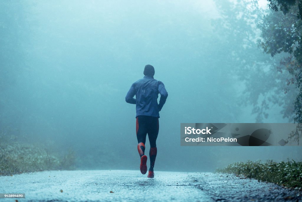 Motivated young man running in the rain. Motivated young man running in the rain. Rear view. Copy space. Running Stock Photo
