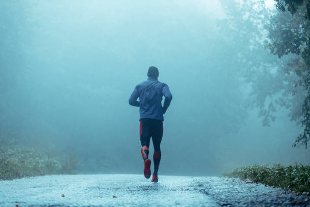 jovem motivado correr na chuva. - running jogging road exercising - fotografias e filmes do acervo