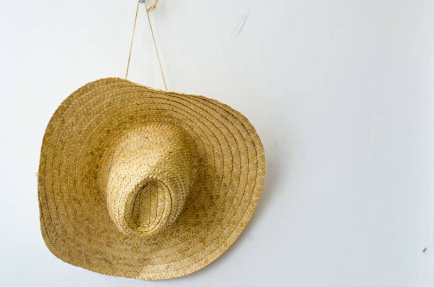 istock Straw hat hanging by a rope on a white wall. 943900364