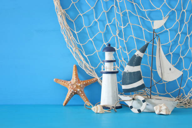 istock nautical concept with white decorative sail boat, lighthouse, starfish, seashells and fishnet over blue wooden table and background. 943909846