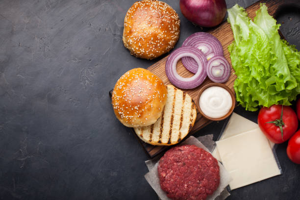 istock Hamburger Building Kit. Fresh ingredients for Burger on dark stone table. Top view with copy space 943910630