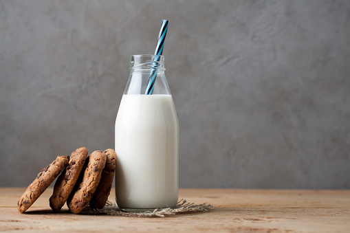 Bottle with milk and chocolate chip cookies on dark background with copy space.