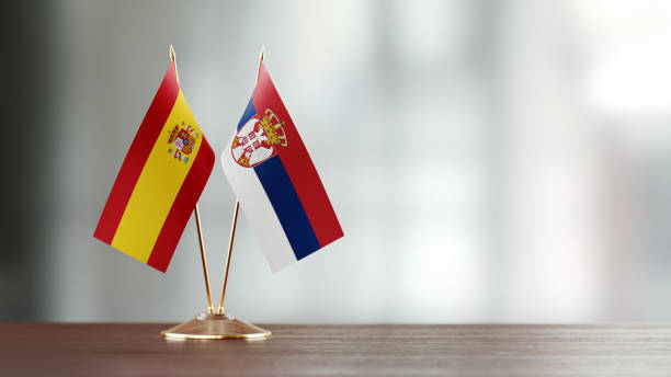 istock Spanish And Serbian Flag Pair On A Desk Over Defocused Background 943917486