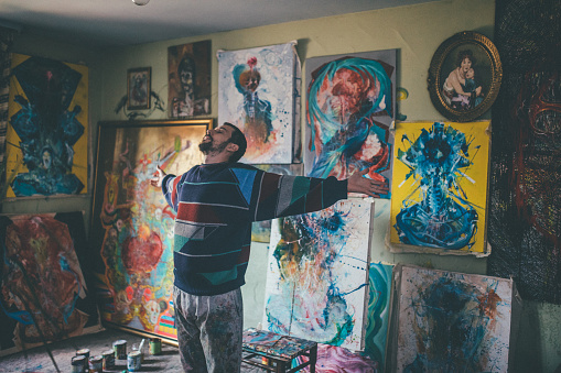 One man, standing in his home studio, paintings all around him.