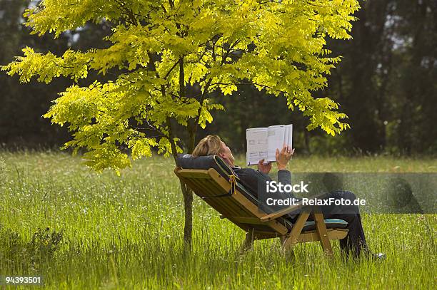 Mature Woman Lying Outdoors In Deck Chair Reading Book Stock Photo - Download Image Now