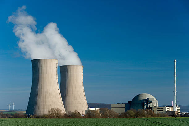 Nuclear power station Grohnde with steaming cooling towers Nuclear power station Grohnde countryside in Lower Saxony, Germany. Two small wind turbines in the Background on the left side of the two cooling towers. Useful as a symbol for the power structure between atomic and alternative energy. nuclear energy stock pictures, royalty-free photos & images