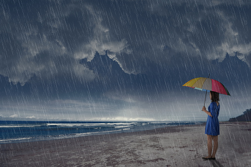 Young asian woman with umbrella looking at ocean view at rain