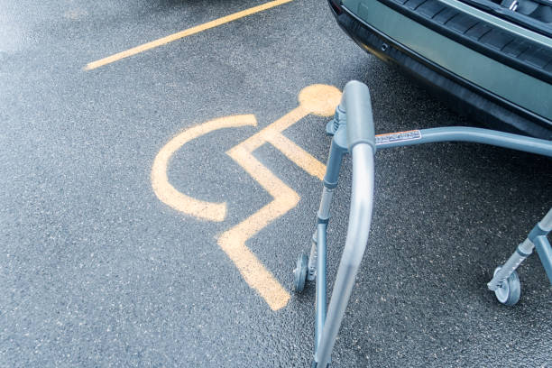 A senior adult mobility walker is waiting to be folded up and put into the back hatch of a car parked in a slippery, wet, designated handicapped parking lot space.\n\nMobility Walker Behind Car in Handicapped Parking Lot Space