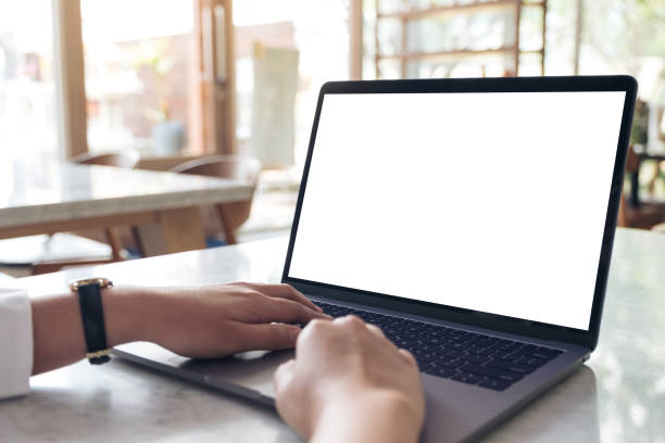 istock Mockup image of hands using and typing on laptop with blank white desktop screen on table in modern cafe 943946436